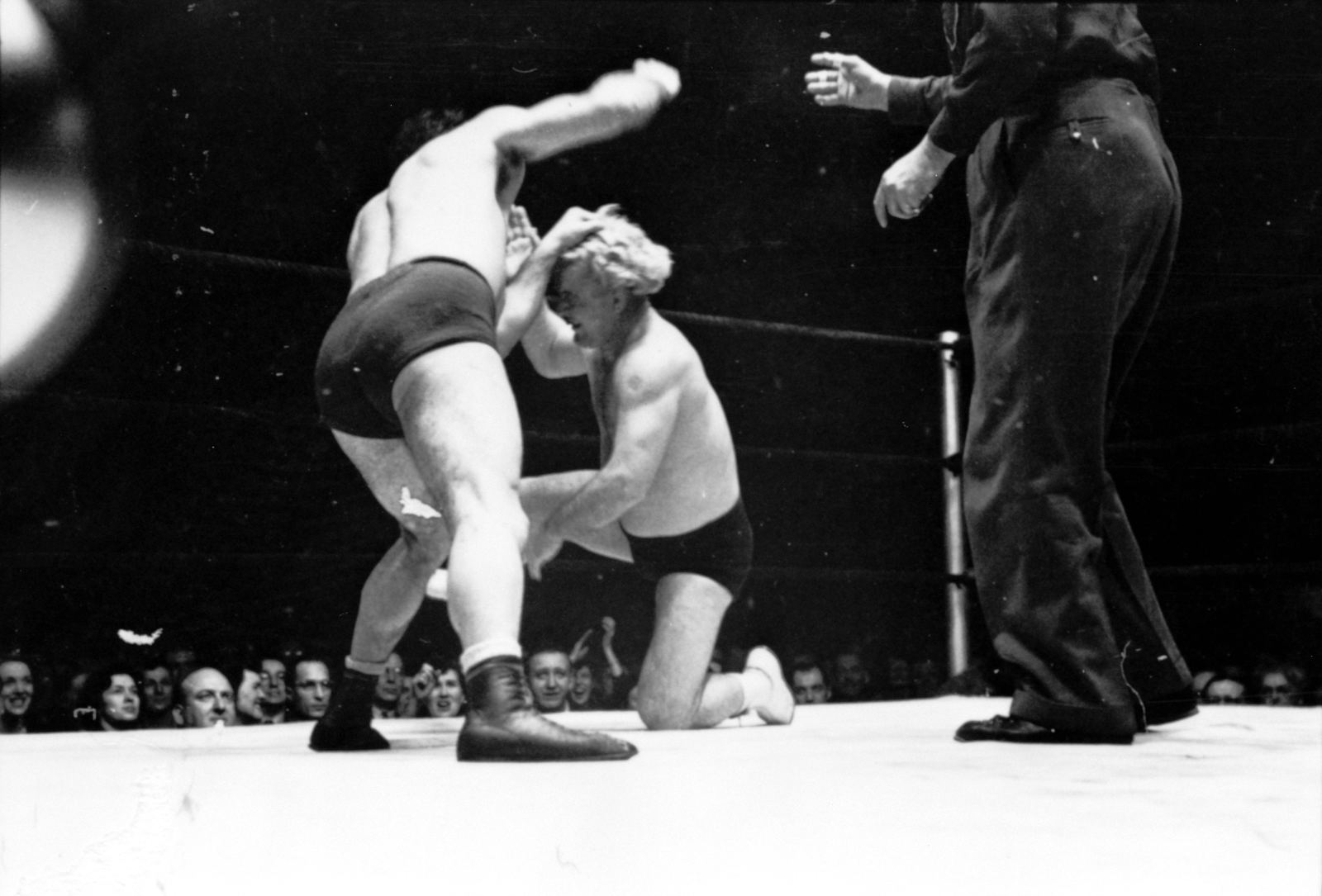 Black and white 1949 photo of Gorgeous George kneeling during a wrestling match