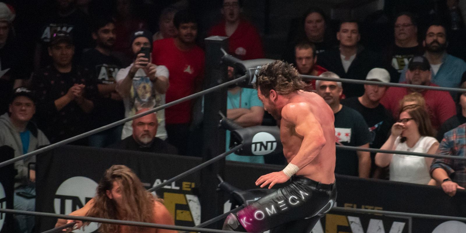 Kenny Omega leaping with a knee strike during a match
