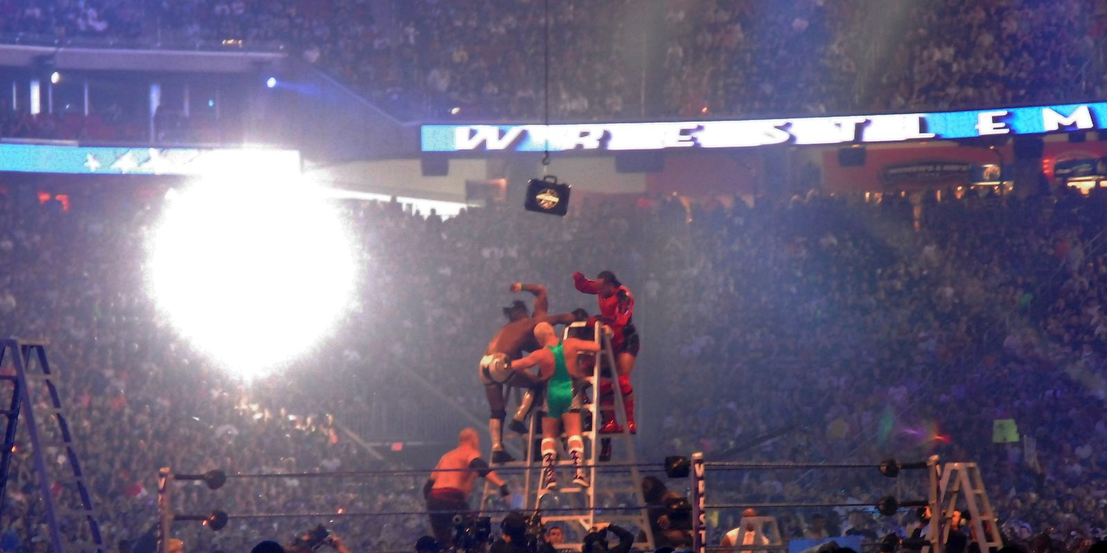 Wrestlers climbing a ladder in the ring to grab a belt hanging above